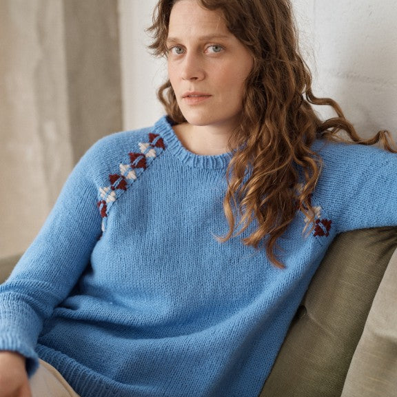 Woman wearing a blue sweater with floral patterns sitting on a couch.