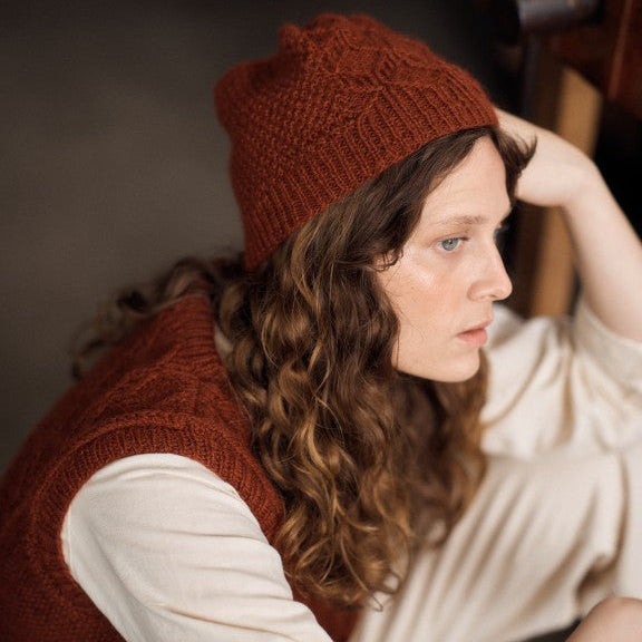Woman wearing a brown knitted hat and vest indoors