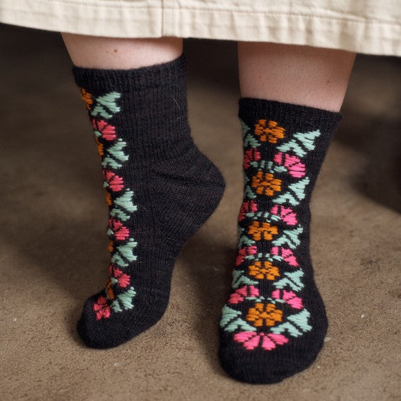Black socks with colorful floral patterns worn by a person, standing on a carpeted floor.