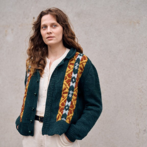 Woman wearing a dark green knitted cardigan with colorful patterns against a plain background