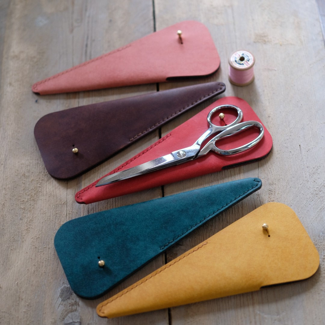 Set of scissors with colorful leather cases on a wooden surface