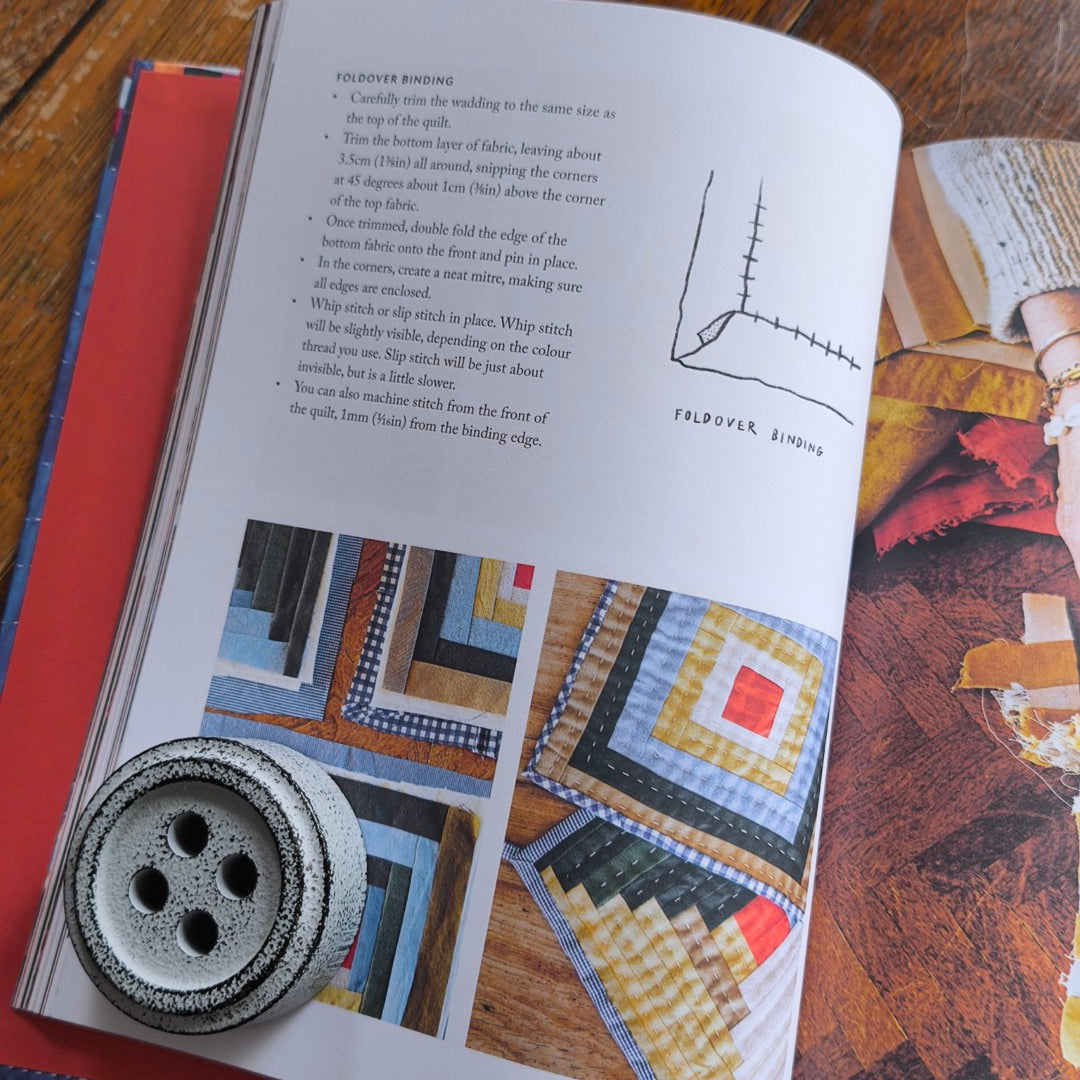 Book open to a page with quilt patterns and a button on a wooden surface