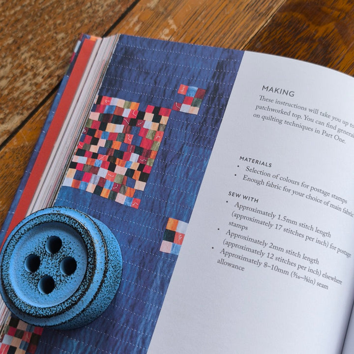 Blue button on an open book with a colorful quilt pattern