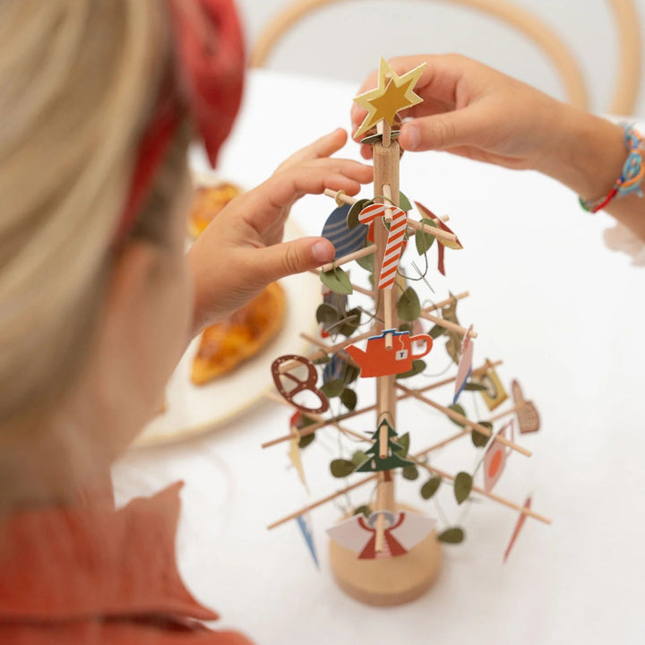 Child decorating a small wooden Christmas tree with ornaments.
