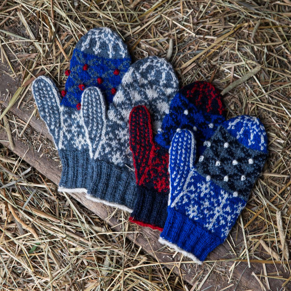 Set of blue, red and white knitted mittens on a straw background
