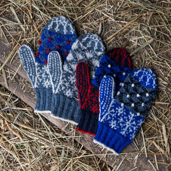 Set of blue, red and white knitted mittens on a straw background