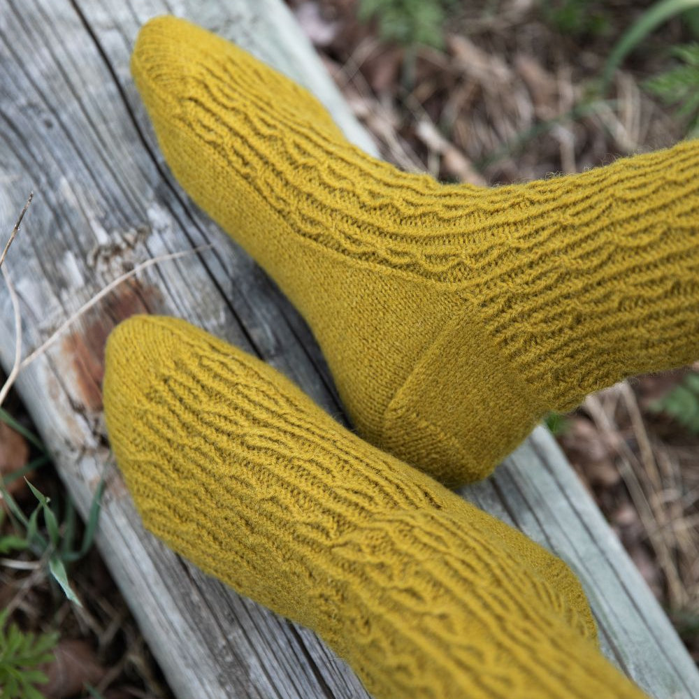 Yellow knitted socks on a wooden log with a natural background