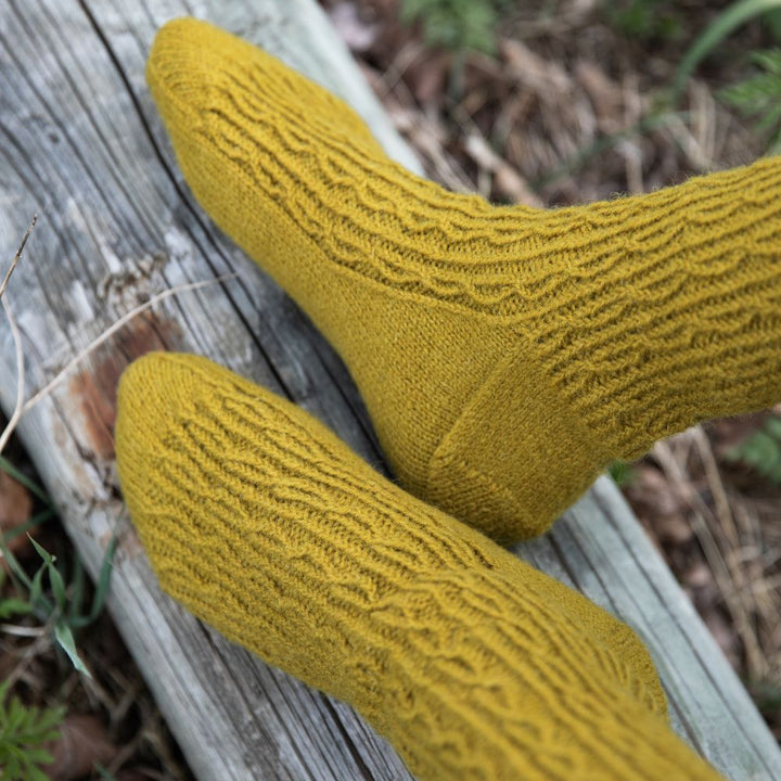 Yellow knitted socks on a wooden log with a natural background
