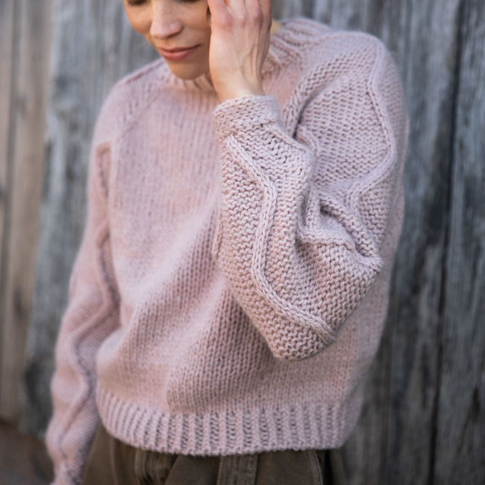 Woman wearing a light pink knitted sweater against a wooden background