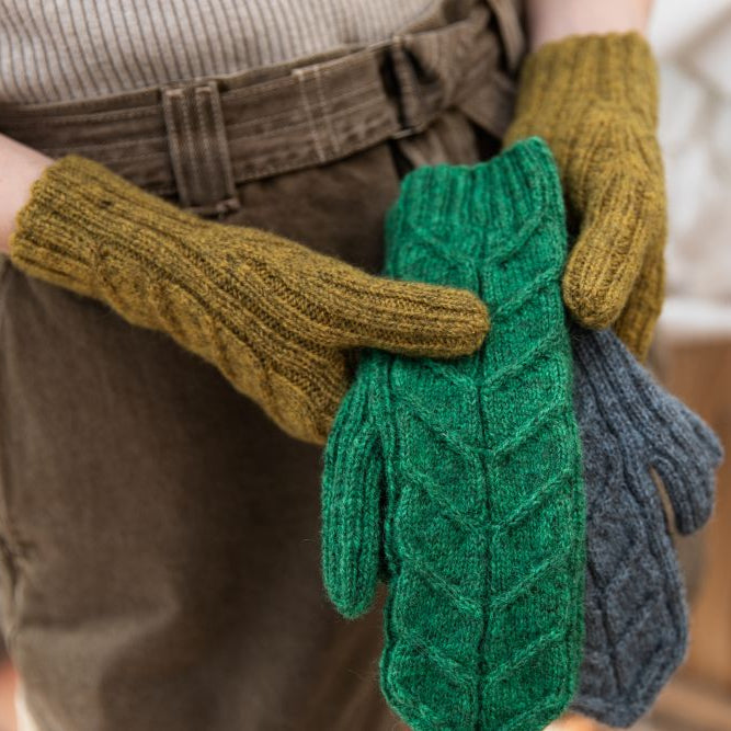 Person holding green and gray knitted mittens outdoors