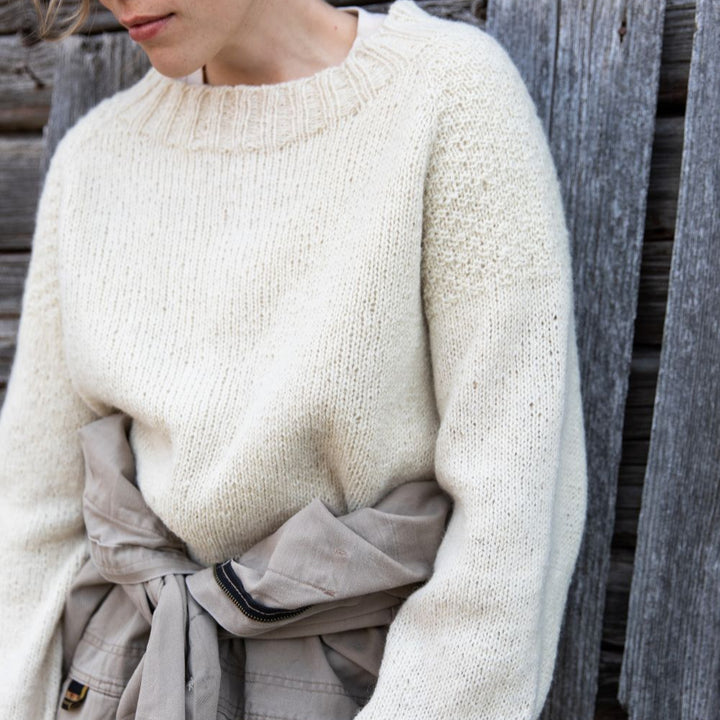 Person wearing a cream textured sweater and beige pants against a wooden background