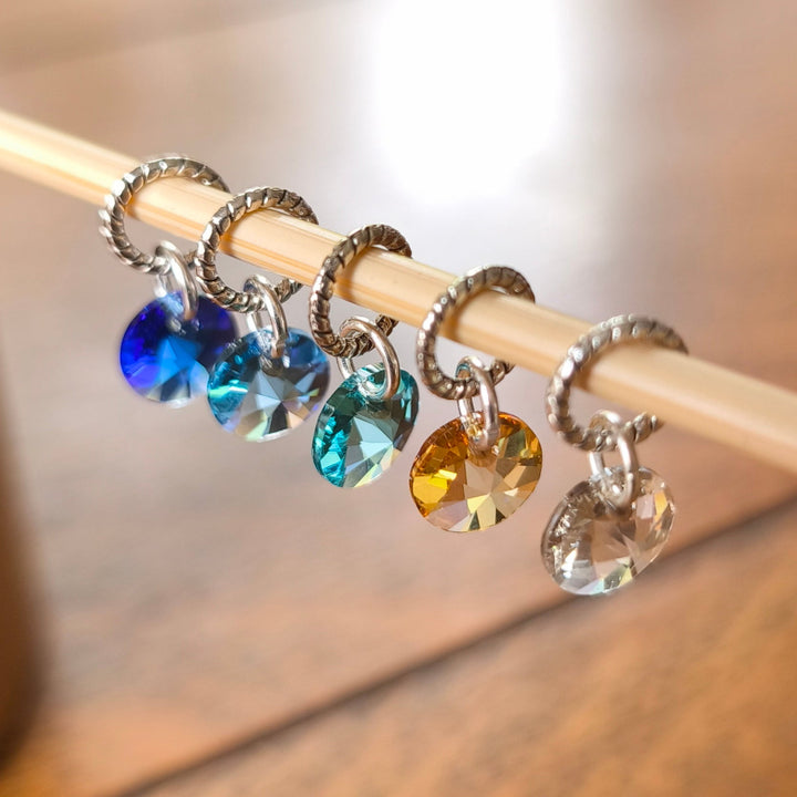 Colorful crystal charms stitch markers on a wooden knitting needle