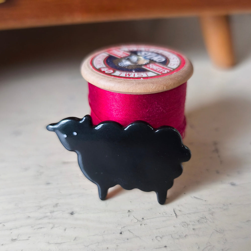 Spool of red thread with a black sheep-shaped brooch on a light wooden surface